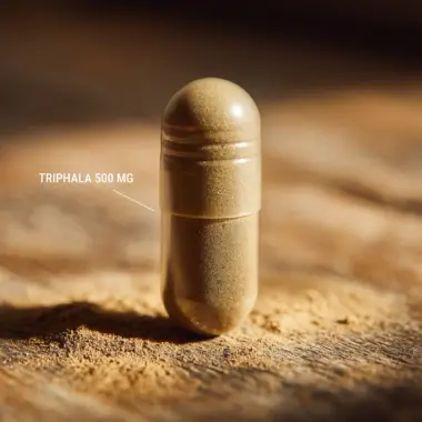 Macro shot of a single Triphala capsule showing the blended herbal fruit powder.